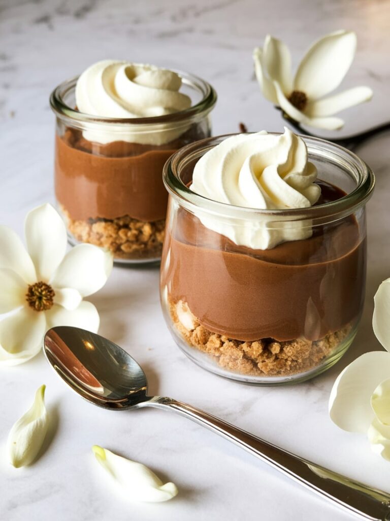 Chocolate pudding pie cups layered with cookie crumbs and topped with whipped cream in small glass jars
