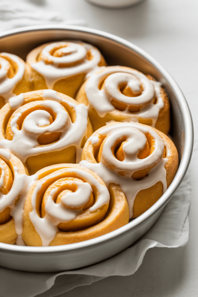 Real-life image of orange sweet rolls, soft citrus desserts swirled with orange sugar and topped with glossy citrus glaze, photographed in a bright white kitchen with soft natural shadows and minimal styling.