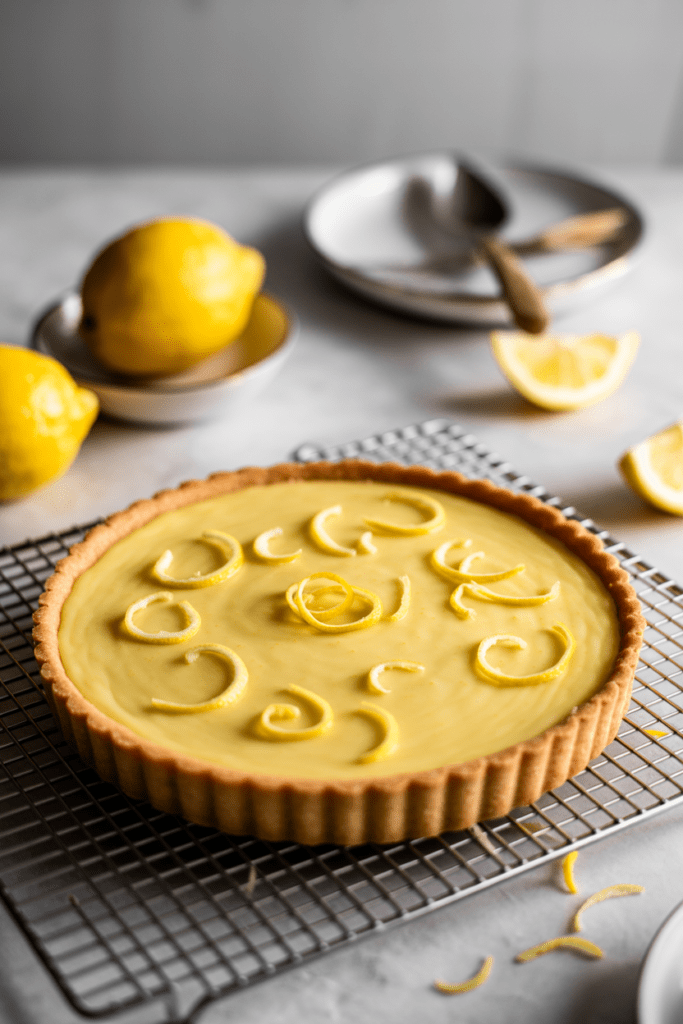 Real-life photo of a lemon tart, a citrus-inspired dessert with smooth yellow filling and crisp edges, styled on a white surface in a bright modern kitchen with soft natural lighting.