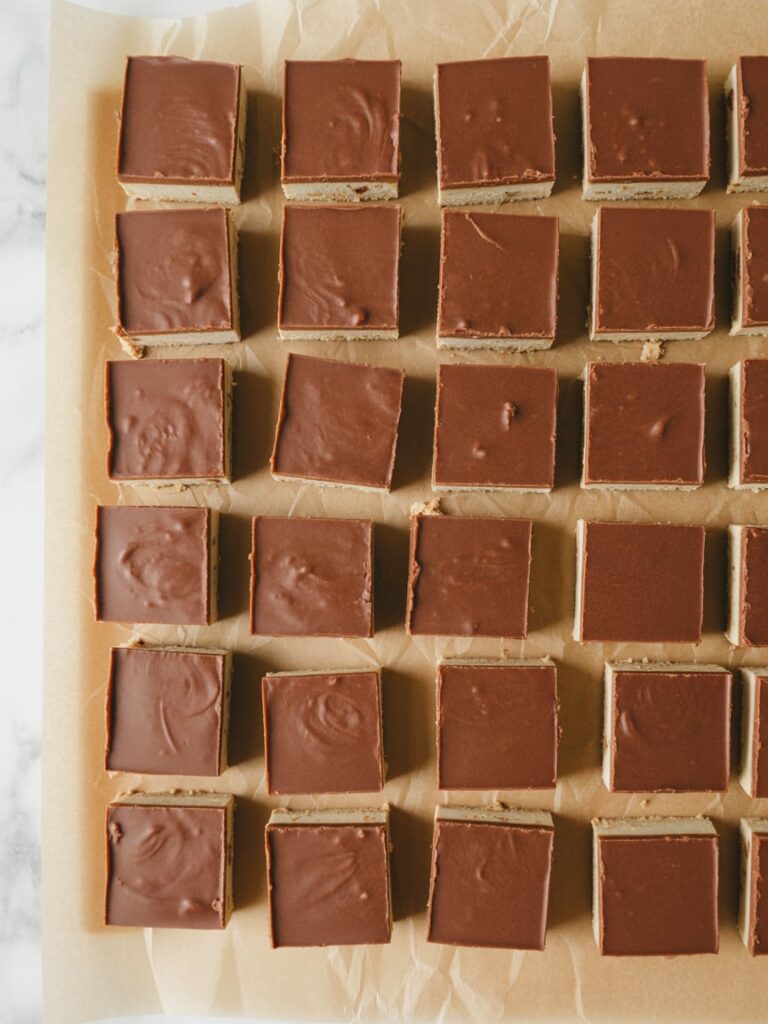 Close-up real life image of sliced dessert bars and fudge arranged uniformly on parchment-lined trays,clean edges,minimal styling,natural light,no text.
