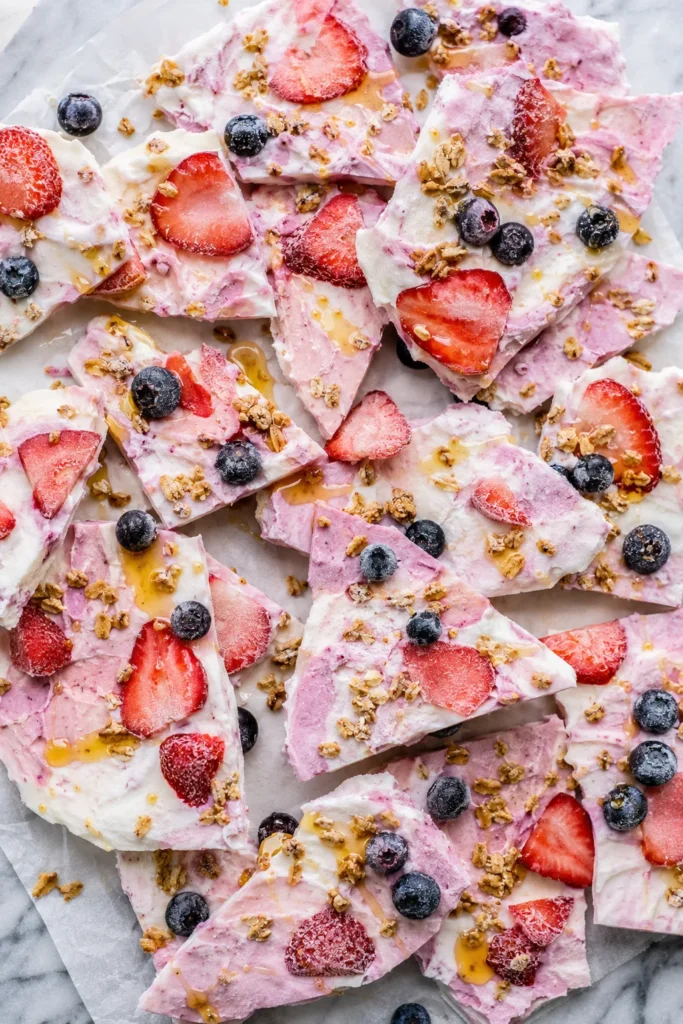 Broken pieces of frozen berry yogurt bark topped with granola and a honey drizzle