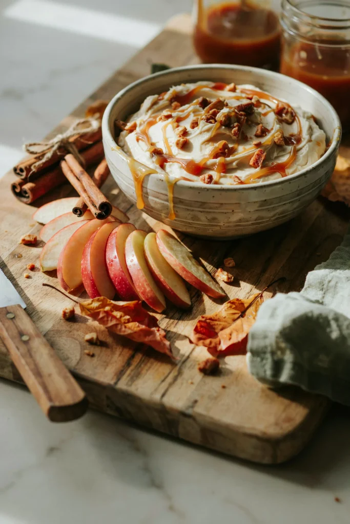 Bowl of swirled caramel apple dip topped with toffee bits and sliced apples for dipping
