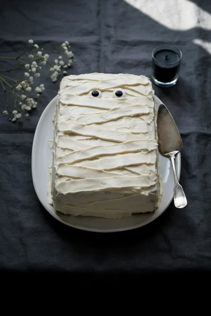 Vanilla sheet cake decorated with piped white buttercream mummy bandages and candy eyes