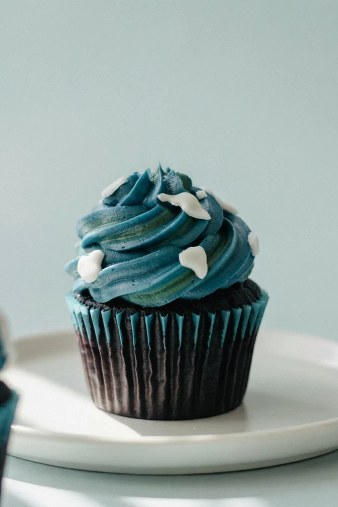 Blue velvet cupcake topped with marbled blue and green buttercream and small white fondant continent shapes