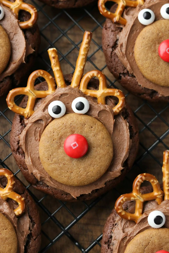 Round chocolate reindeer cookies with pretzel antlers, candy eyes, and a red nose cooling on a wire rack