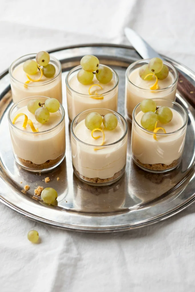 Small mason jars filled with pale, creamy no-bake cheesecake with a hint of gold shimmer, topped with a few champagne grapes.